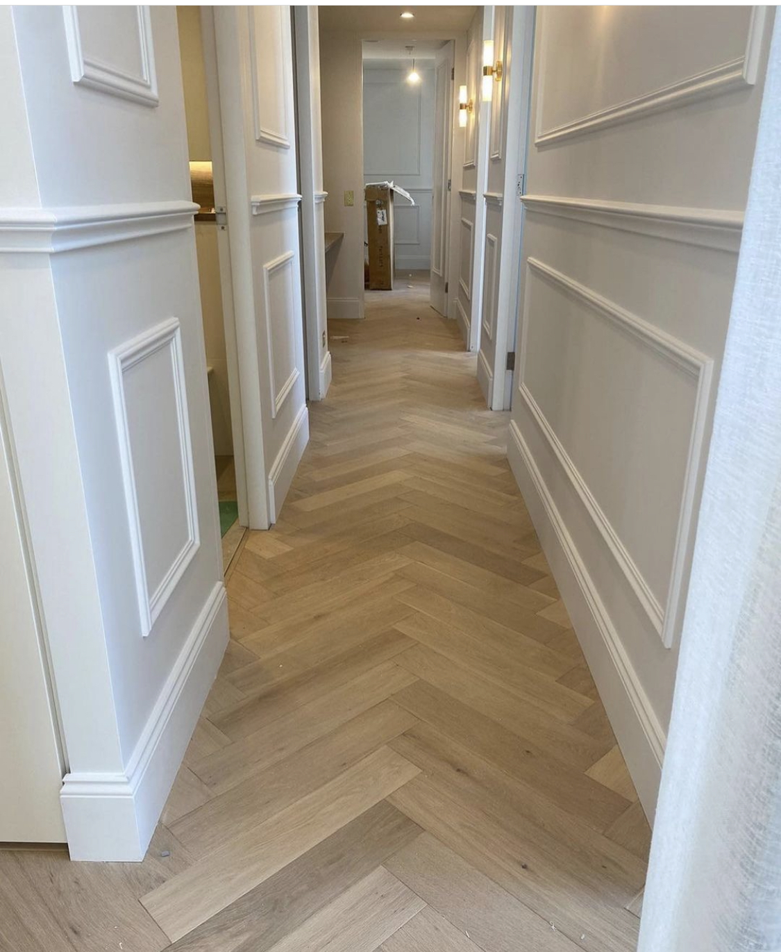 Engineered oak herringbone flooring in a panelled hallway with wall moulding